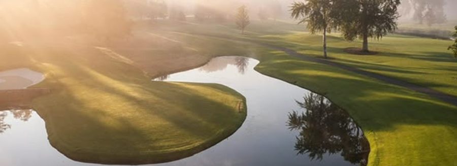 A misty fairway and water hazard lit by low morning sun